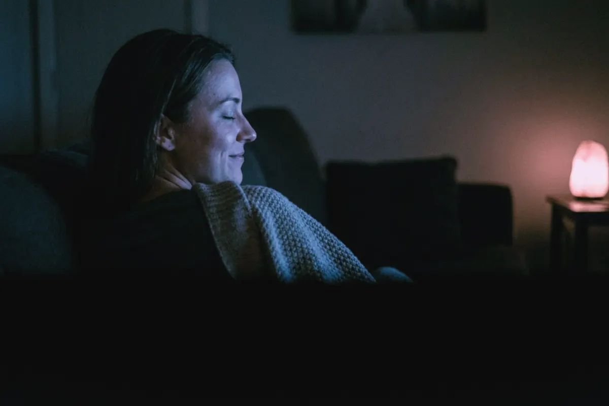 A woman&rsquo;s profile lit by a screen off-frame, eyes closed, beginning to smile